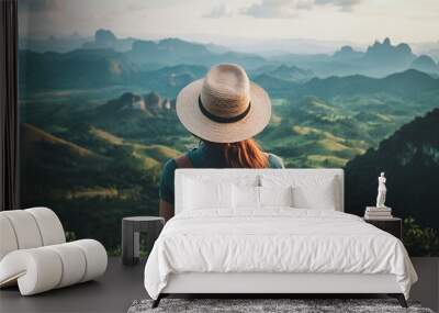 A person with a backpack and hat gazes at a scenic mountain landscape during sunset. Wall mural