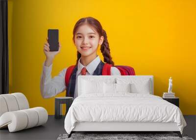 A student in a uniform smiles while holding a smartphone against a bright yellow background. Wall mural