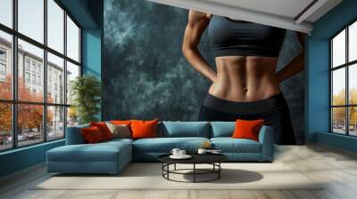 Close-up of a woman's toned abs and waist in a black sports bra and leggings, against a dark smoky background. Wall mural