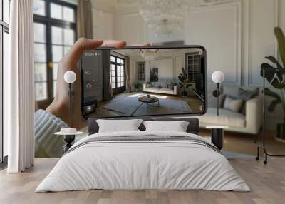 Person using a mobile phone to view a virtual tour of a living room, featuring a white couch, a coffee table, a house plant, and an elegant chandelier. Wall mural