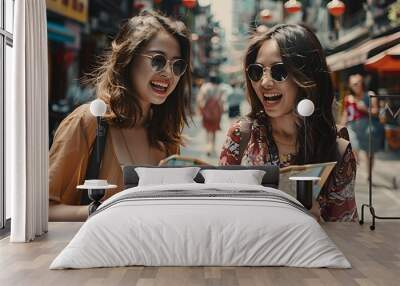 Two young women wearing sunglasses, smiling and looking at a map while standing on a busy street in an Asian city. Wall mural