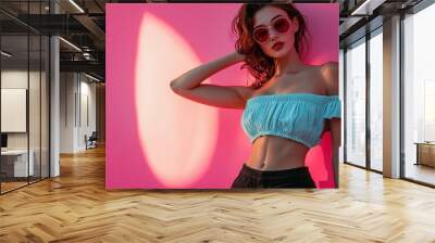 Stylish woman in sunglasses and summer attire posing against a pink background Wall mural