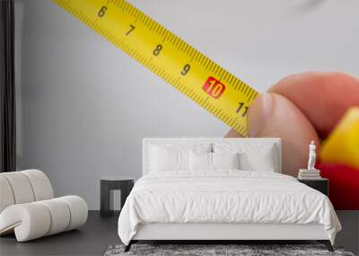 A close up of a yellow metric tape measure with a white hand holding it close for precision. Wall mural