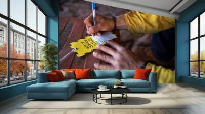 Safe workplaces practices construction worker wearing long sleeve shirt using a blue pen writing on yellow out of service tag prior tagging on damaged faulty goods equipment      Wall mural