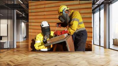 Safety workplace welder supervisor wearing dark shield mask welding PPE teaching guiding inspecting new worker on site while co worker welder is welding repairing chute liners Australia mining site Wall mural