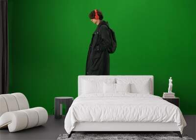 Portrait of person tourist isolated on chroma key green screen background. Young man in coat and headphones walking and listening music. Wall mural