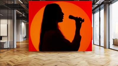 Stylish young woman black silhouette in casual clothing singing song in karaoke microphone. Isolated on red studio background spotlight. Wall mural