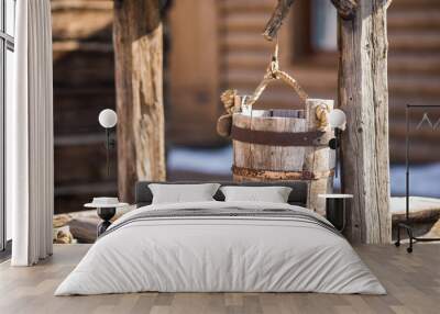 old wooden bucket of water hanging over the well with a wooden building Wall mural