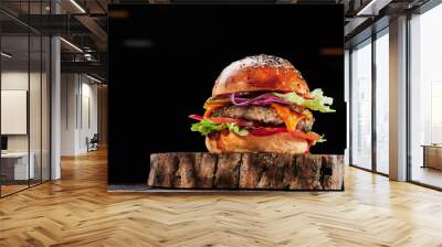 Beef burger with cheese, tomatoes, red onions, cucumber and lettuce on wooden cut on black background. Burger menu. Space for text. Unhealthy food. High quality photo Wall mural