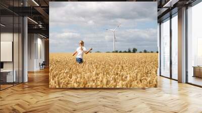 Back view little cute happy blond caucasian girl enjoy walking ripe wheat ear field against wind mill turbine farm on warm sunny summer day. Child freedom future clean energy environment concept Wall mural