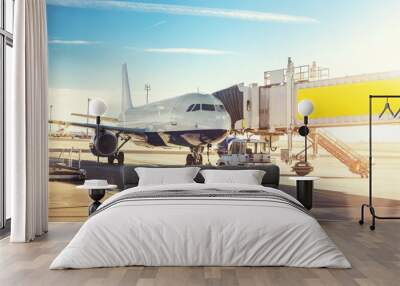 Big modern commercial plane on airfield docked with boarding bridge at sunrise or sunset. Blue clear sky on background. Travel and tourist destination concept Wall mural