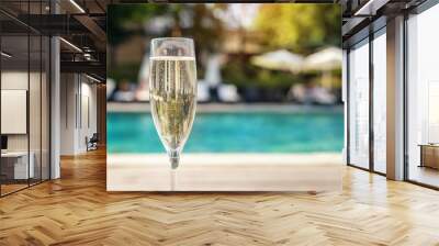 Close-up white champagne or prosecco glass against poolside at luxury resort hotel during vacation. Sparkling wine with rising bubbles with blue pool background outdoor. Refreshing alcohol drink Wall mural