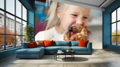 Cute adorable caucasian blond little girl portrait enjoy eating roasted turkey shank at dinner at restaurant or cafe indoors. Happy small hungry kid biting fat big meat. Children healthy diet Wall mural