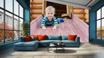 Cute adorable caucasian toddler boy having fun sliding down wooden slide at eco-friendly natural playground at backyard in autumn. Playful funny child portrait enjoying outdoor sport acitivities Wall mural