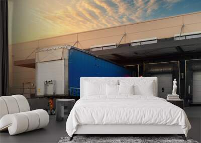 Innovative modern logistics warehouse center complex building exterior bay gate semi-trailer unloading goods distribuition warm blue sunset sky background. Cargo storage facility industry building Wall mural