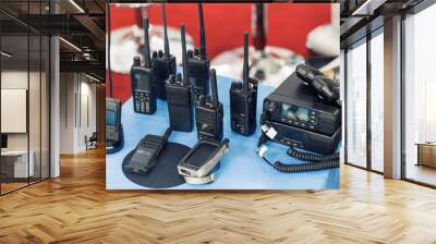 Many portable radio transceivers on table at technology exhibition. Different walkie-talkie radio set. Communication devices choice for military and civil use Wall mural