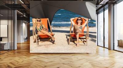 Pair of young adult slim sporty fit woman friends enjoy relax chilling and sunbathing on loungers on send ocean sea beach at exotic resort. Sunscreen protection. Summer travel vacation concept Wall mural