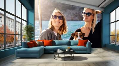 Portrait two young adult beautiful pretty caucasian woman enjoy sailing family cute adorable little jack russel dog on yacht boat against blue water bright summer day. Travel sea tourism with pets Wall mural