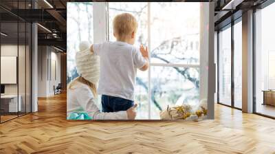 Two cute adorable little blond cauasian children siblings stay near window and looking outside waiting for snow, wonders and miracle at christmas holidays. Stay home at covid-19 pandemic lockdown Wall mural