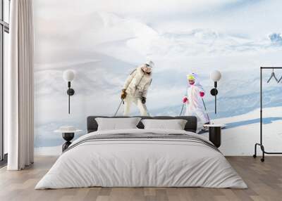 Young adult beautiful sporty mother having fun skiing with kid daughter on mountain alpine ski winter resort. Slim mom in luxury fashion skier suit and child enjoy outdoor recreation activities Wall mural