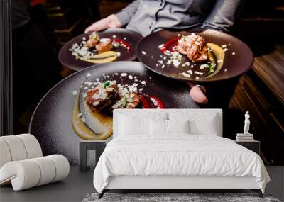 The girl waiter carries three plates of food. Meat steak garnished with two sauces on a dark plate. Close-up. Wide angle photography.  Wall mural