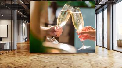 two girls clink glasses of champagne on a beautiful summer terrace. sparkling champagne glasses Wall mural