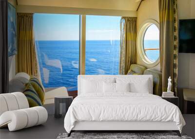 A bowl of fruit sits on a table in a luxury cruise ship cabin with a large window and porthole to balcony as it sails on a blue Mediterranean Sea. Wall mural