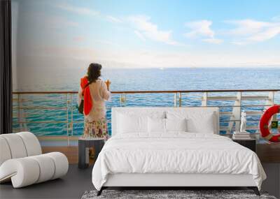 A dark haired woman on enjoys a drink on the deck of a cruise ship passing through the Greek Islands at sunset Wall mural