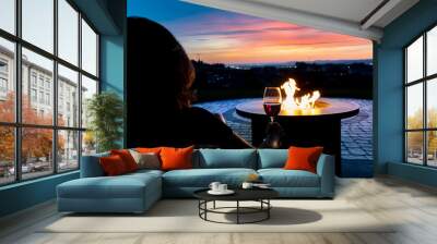 A woman relaxes with a glass of wine at sunset by a fire pit on the patio of a luxury home overlooking the Spokane valley and city in Spokane, Wa USA Wall mural