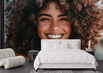  Radiant close-up of a young woman with curly hair, smiling joyously as she touches her lush locks. Wall mural