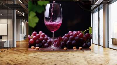 A wine glass filled with red wine surrounded by grapes and other fruits on a dark surface indoors. Wall mural