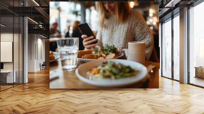 Woman sitting at table, phone in hand. Wall mural