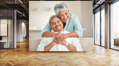 Senior couple, sofa and portrait with hug, smile and love in home living room with care, romance and happiness. Elderly man, old woman and embrace by lounge couch in retirement together in house Wall mural