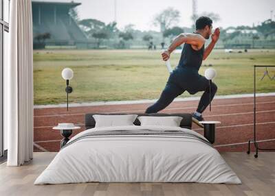 Stadium, man relay running and athlete on a runner and arena track for sprint race training. Fast, run and sports exercise of a male person in marathon for fitness and workout outdoor on a field Wall mural