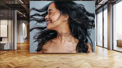 Her hair has natural bounce and great volume. Studio shot of an attractive young woman tossing her hair against a grey background. Wall mural