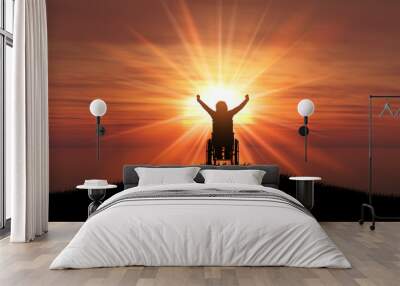 3D silhouette of a female in a wheelchair with her arms raised against a sunset ocean Wall mural