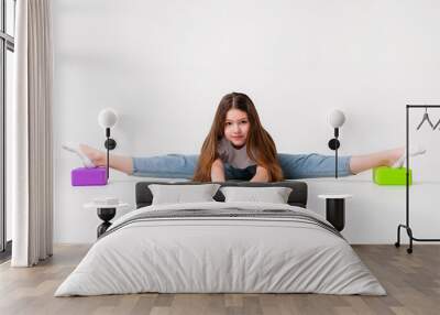 A teenage girl in jeans and a white t-shirt stretches her legs with green and purple styrofoam cubes. White background. The concept of sports, yoga. Wall mural