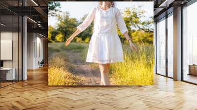 Caucasian happy girl in a white dress with a wreath of wild flowers in the summer at sunset in the field. Wall mural