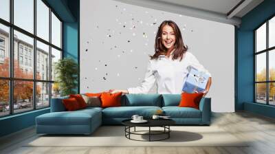 Beautiful happy woman with gift box at celebration party with confetti falling everywhere on her. Birthday or New Year eve celebrating concept Wall mural