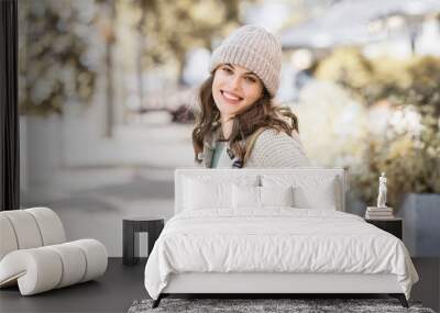 Beautiful joyful woman autumn portrait. Smiling student girl wearing warm clothes and hat in a city in winter Wall mural