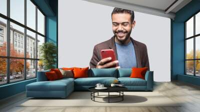 Portrait of handsome cheerful smiling young man using smartphone isolated on gray background. Laughing joyful men with mobile phone studio shot Wall mural