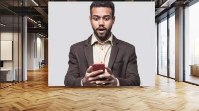 Portrait of handsome cheerful surprised young man using smartphone isolated on gray background. Laughing joyful men with mobile phone studio shot Wall mural