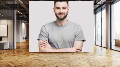 Portrait of handsome smiling young man with folded arms. Smiling joyful cheerful men with crossed hands studio shot. Isolated on gray background Wall mural