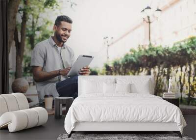 Smiling man student using digital tablet in a city. Young handsome men having coffee break. Modern lifestyle, connection, business, freelance work concept Wall mural