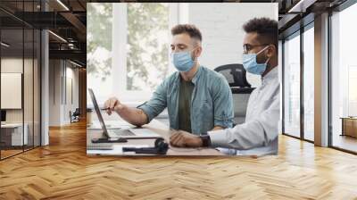 Working moments. Group of young coworkers people discussing business ideas while working in the office. Colleagues have discussion wearing medical protective masks, social distancing concept Wall mural