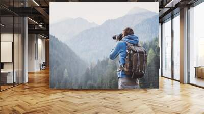 Young cheerful man photographer taking photographs with digital camera in a mountains. Travel and active lifestyle concept Wall mural