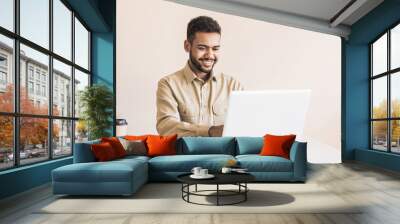 Young handsome man using laptop in office. Businessman or student working on computer online. Freelance, online marketing, education and technology concept Wall mural