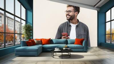 Young handsome man using smartphone in a city. Smiling student men texting on his mobile phone isolated portrait. Modern lifestyle, connection, business concept Wall mural