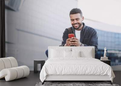 Young handsome men using smartphone in a city. Smiling student man texting on his mobile phone. Coffee break. Modern lifestyle, connection, business concept Wall mural