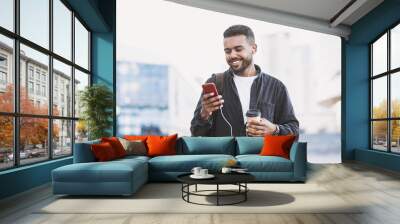 Young handsome men using smartphone in a city. Smiling student man texting on his mobile phone. Coffee break. Modern lifestyle, connection, business concept Wall mural